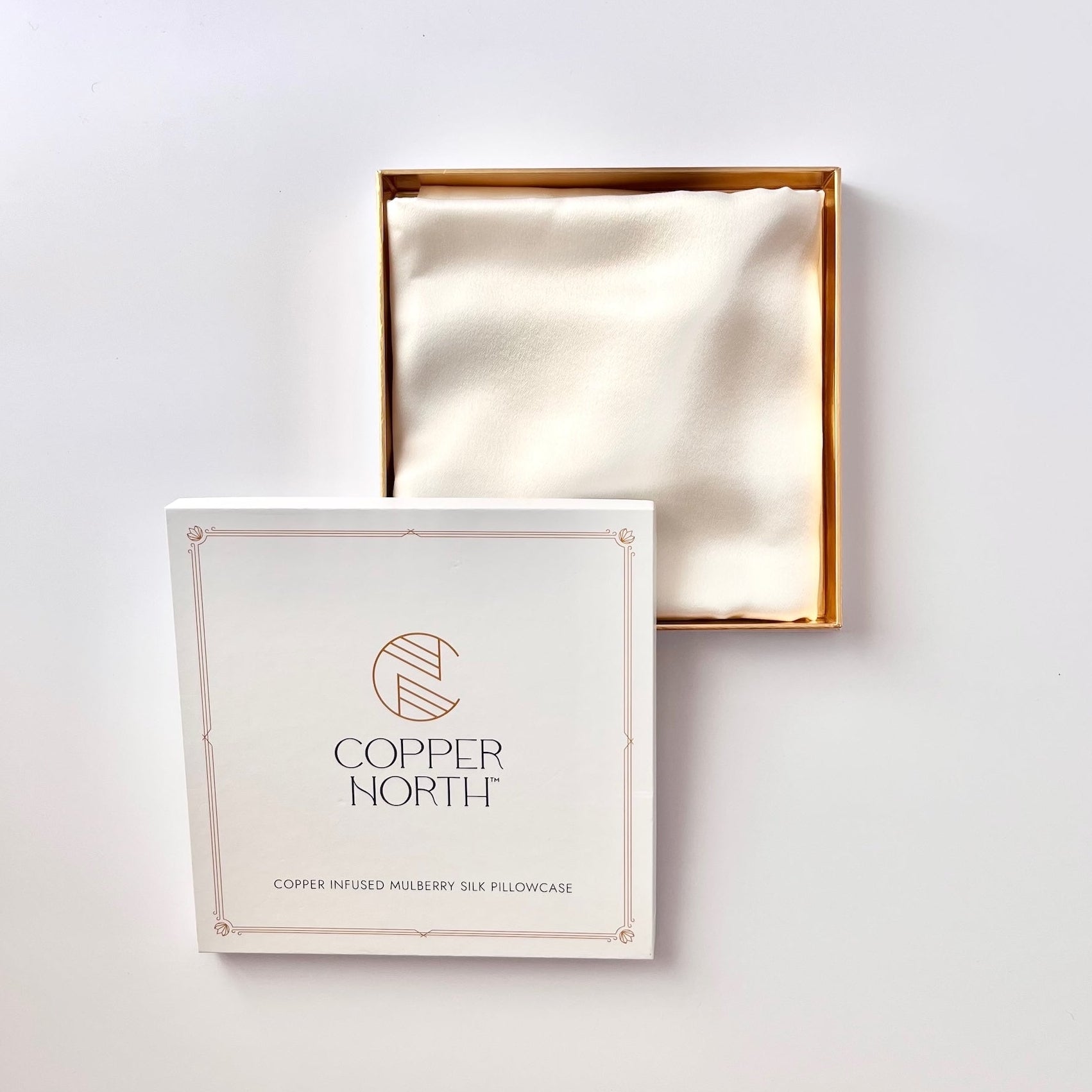 A white square product box labeled 'COPPER NORTH' with a gold-toned logo, shown in front of an open matching box containing a creamy white silk insert, against a plain light background.