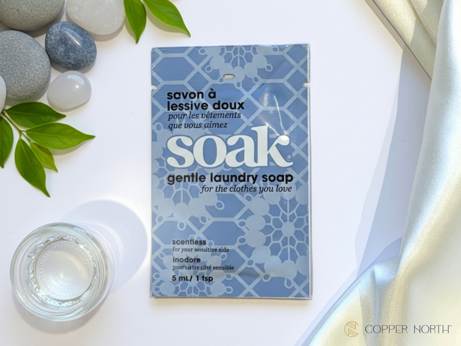 Mini-size of Soak Scentless gentle laundry soap on a white surface with stones and leaves.