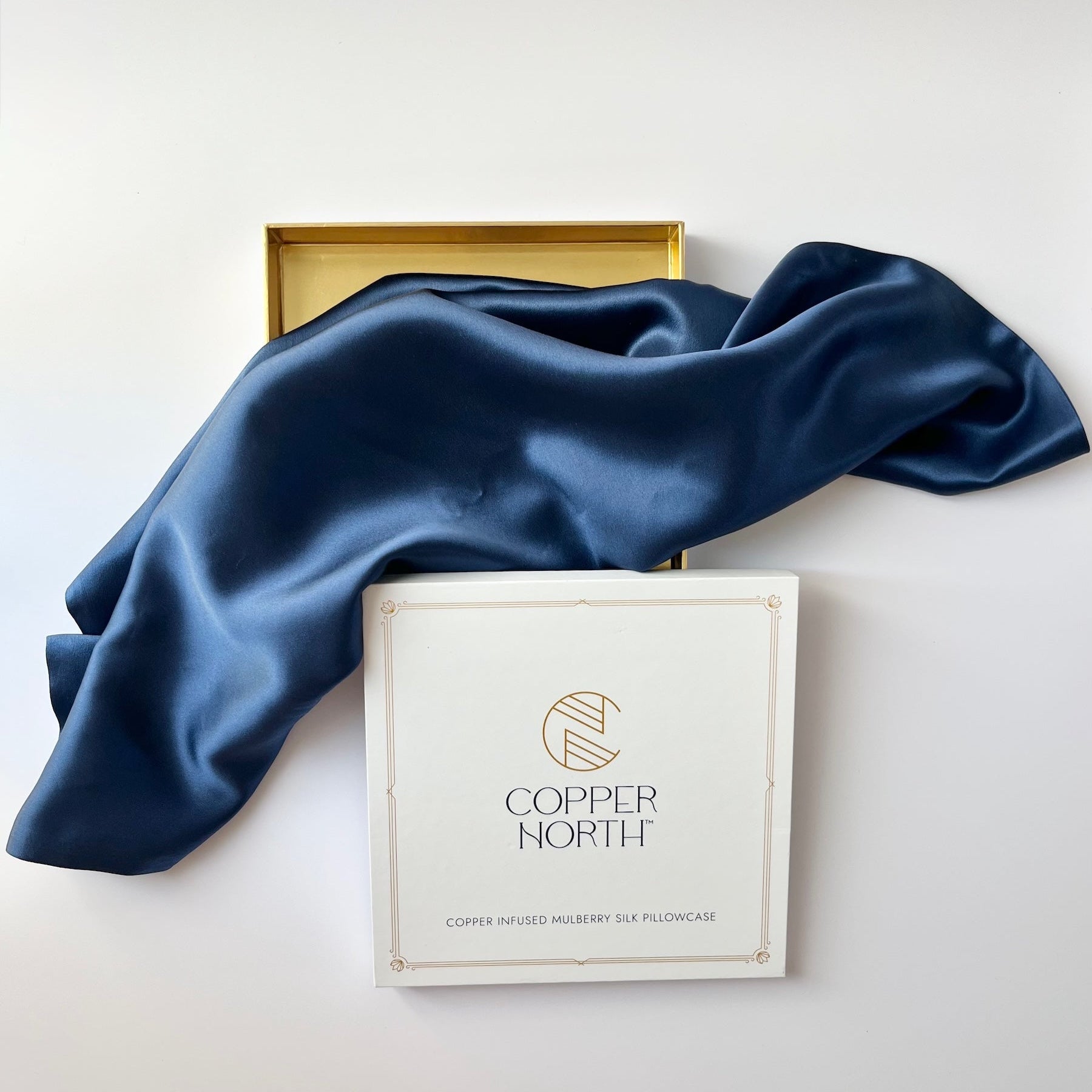 Deep blue silkdraped over a white branded box labeled Copper North, with a gold tray partially visible behind it on a clean white background.