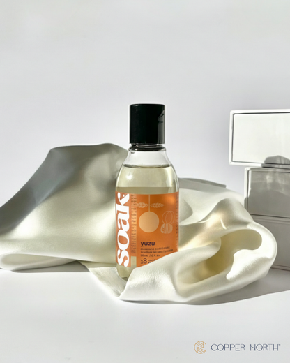 Bottle of Soak Yuzu travel soap on a white surface with a gray background